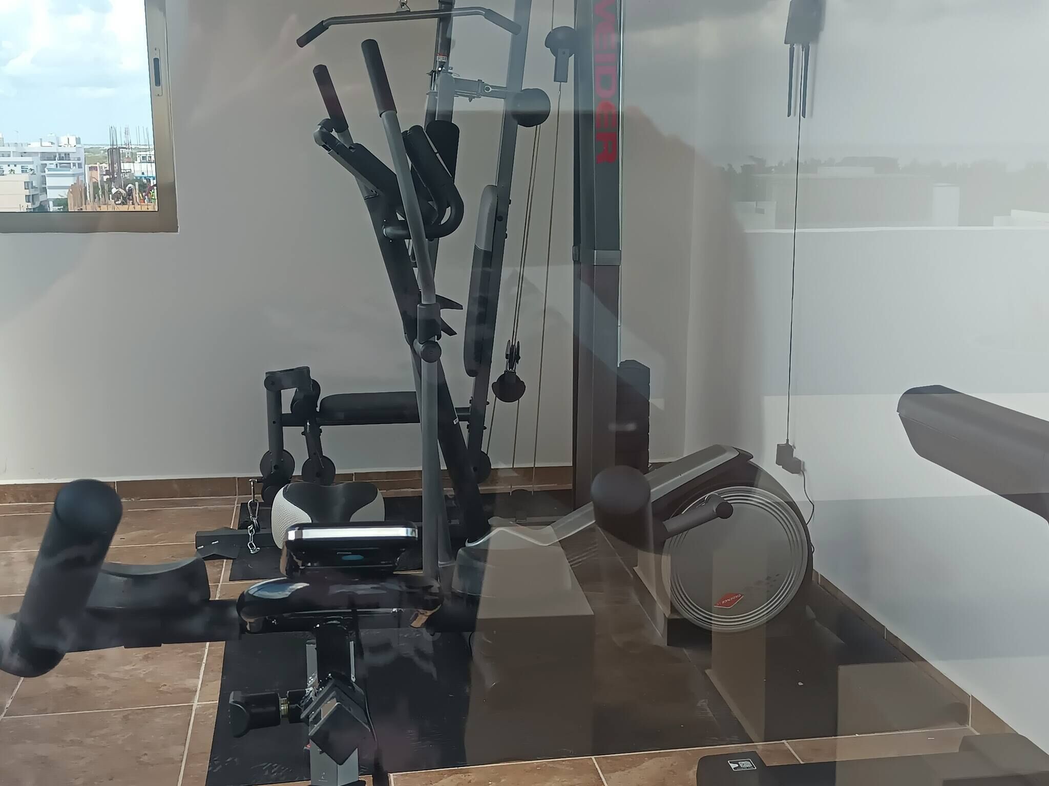 A gym with exercise equipment, a fan, and a window with a city view.