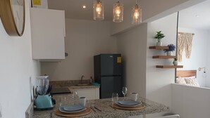 Une cuisine moderne avec des comptoirs en granit, un réfrigérateur noir et un coin repas avec des chaises blanches et une table dressée pour deux personnes.
