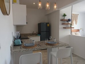 Una cocina moderna con encimeras de granito, un refrigerador negro y un comedor con sillas blancas y una mesa dispuesta para dos.