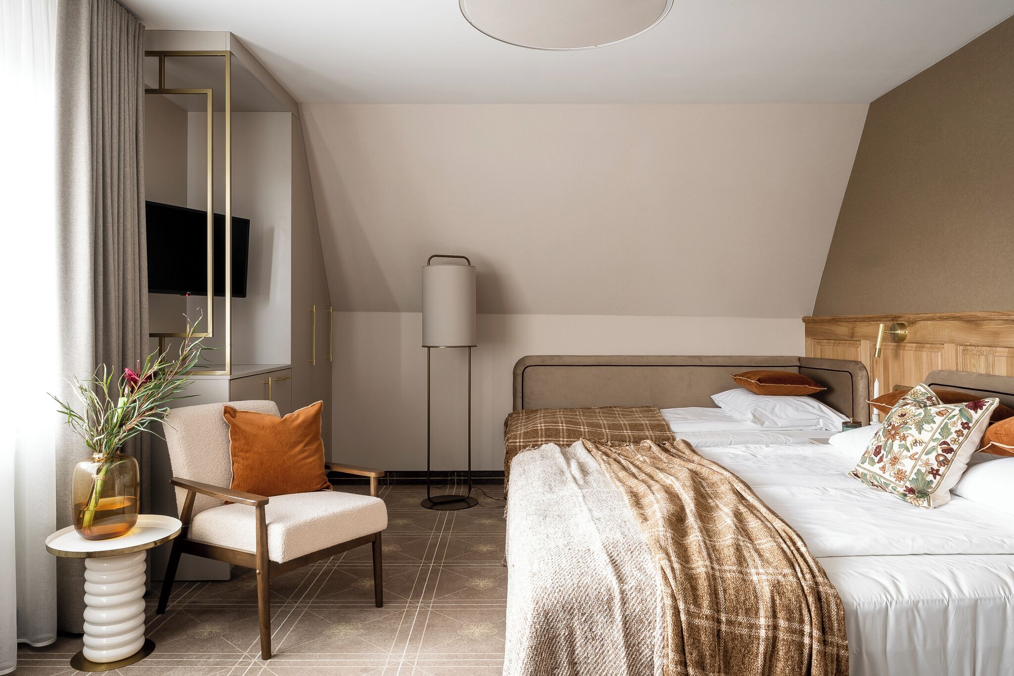 Habitación de hotel moderna con cama, una silla, una mesita auxiliar, una lámpara de pie y un televisor montado en la pared.