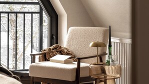 Une pièce confortable avec un plafond haut, une grande fenêtre, un fauteuil, une petite table et un radiateur.