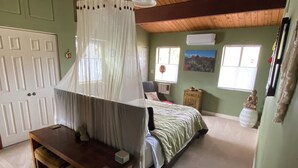 A bedroom with a canopy bed, a wooden desk, a nightstand, a small cabinet, and a wall-mounted air conditioner.