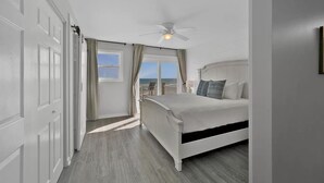 Une chambre avec un lit, un ventilateur de plafond et une vue sur l’océan par la fenêtre.