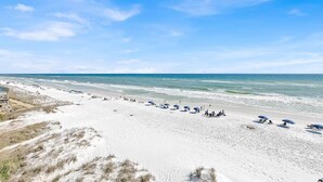 Une plage de sable blanc, un ciel dégagé et quelques parasols.