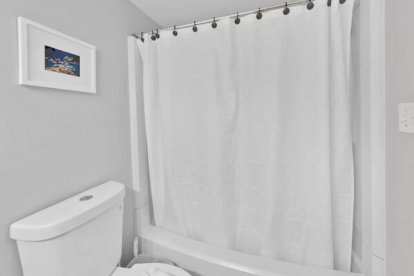 Ein Badezimmer mit einer weißen Toilette, einer Duschvorhang und einem gerahmten Bild an der Wand.