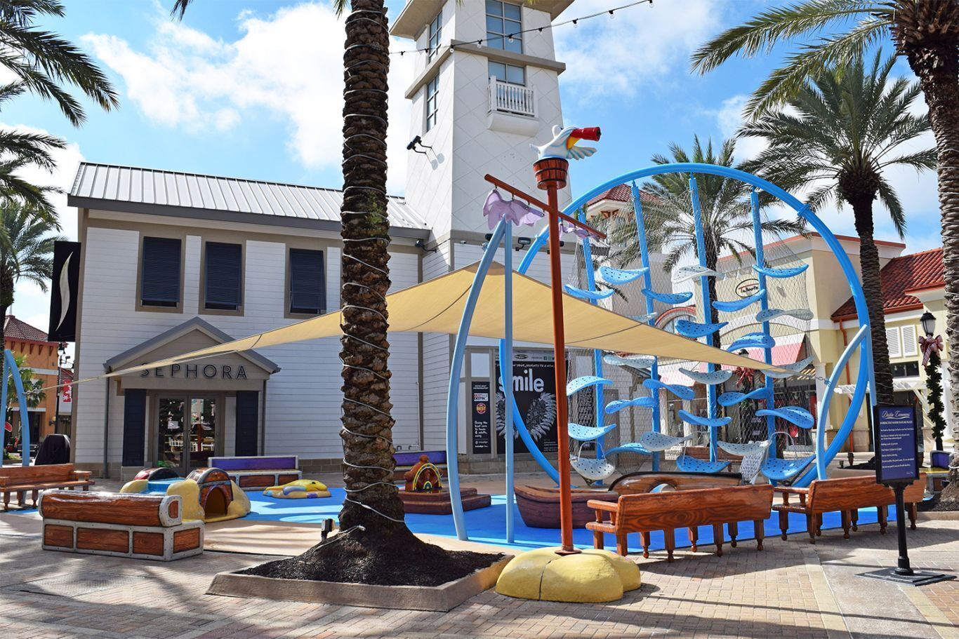 A water park with a play structure, benches, and a Sephora store in the background.