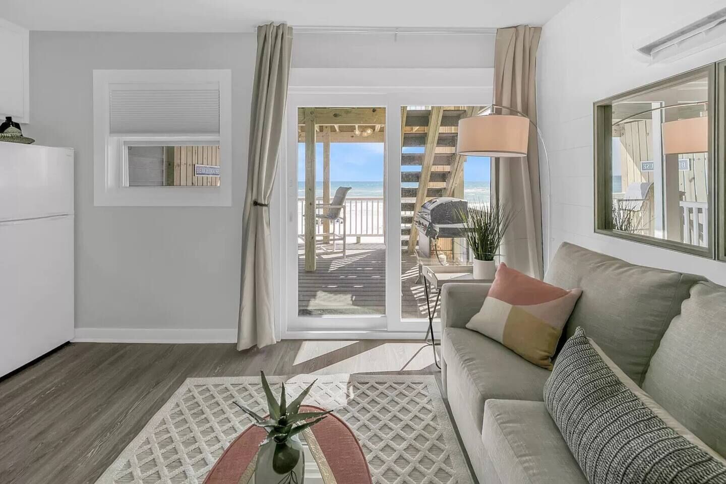 A modern living room with a sofa, a coffee table, and a view of a wooden deck and beach.