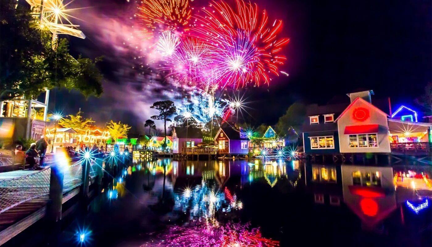 A nighttime scene with a water body reflecting colorful lights and fireworks.