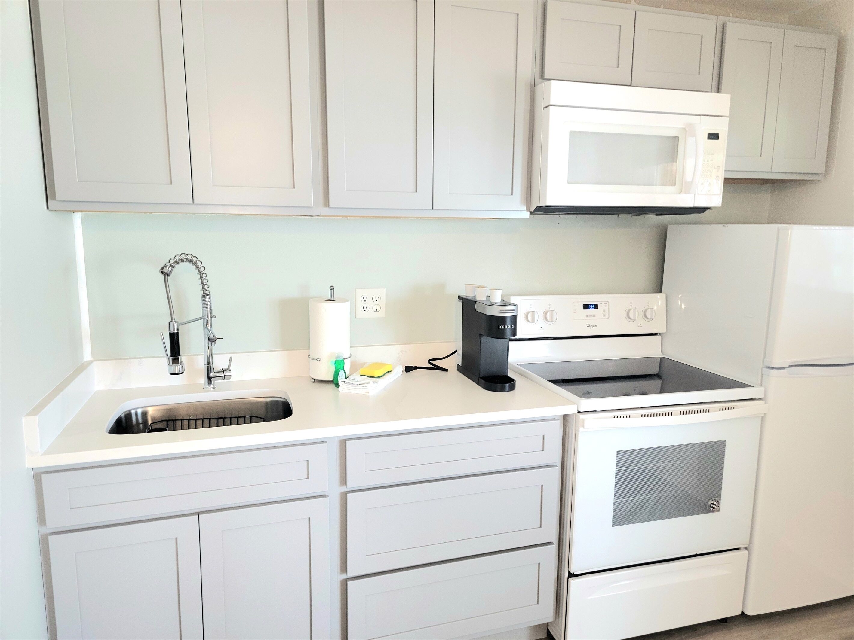 A kitchen with white cabinets, a stainless steel sink, a microwave, a coffee maker, and a built-in oven.