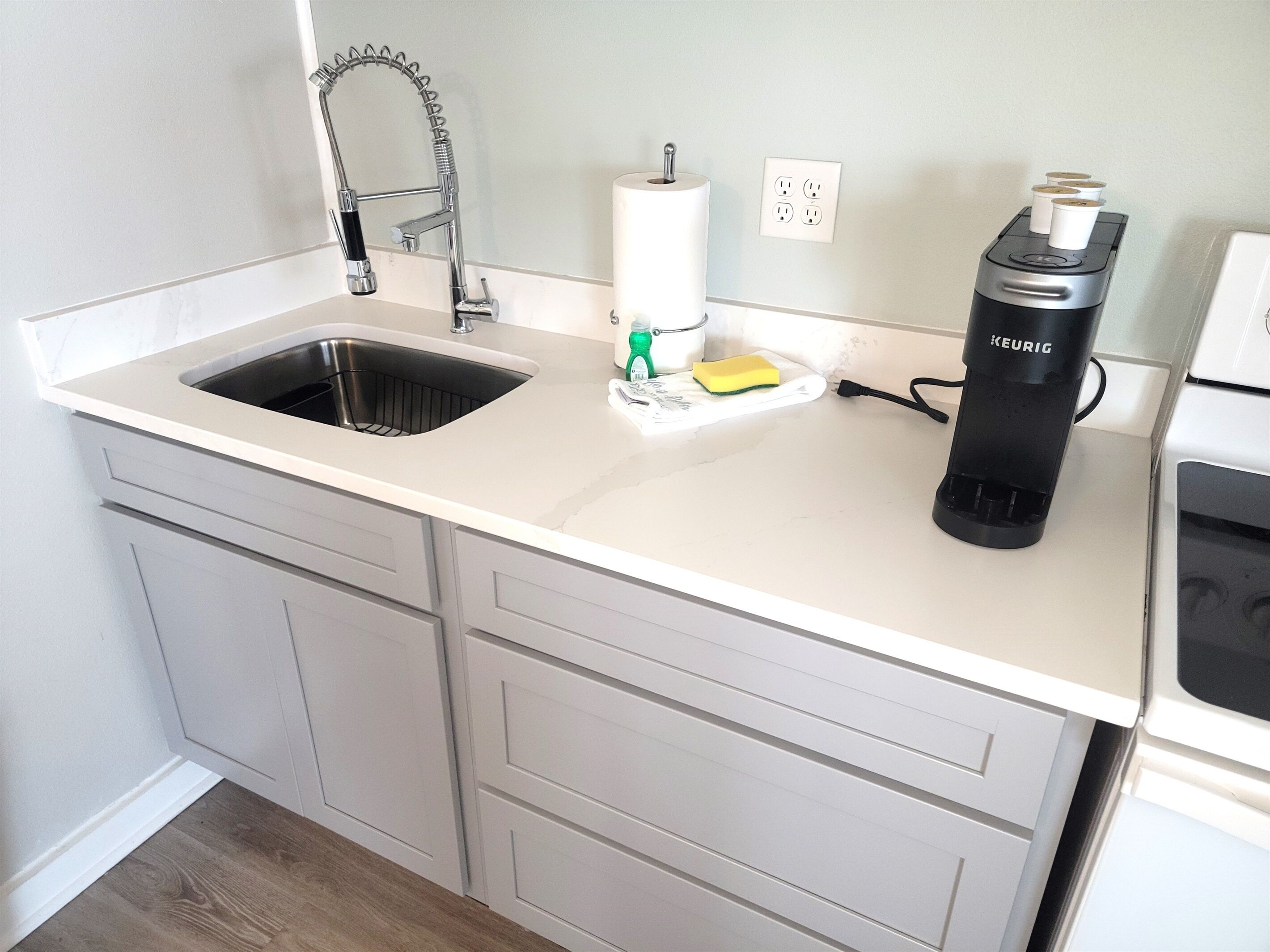 Une cuisine équipée d’un évier en acier inoxydable, d’une machine à café Keurig, d’un rouleau d’essuie-tout et d’une éponge posée sur le comptoir.