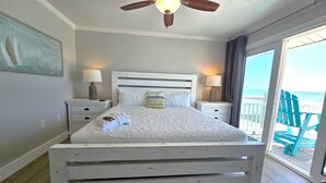 Camera da letto con un letto grande, due comodini, una ventola a soffitto e vista sulla spiaggia.