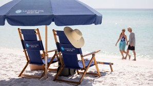 Due sedie da spiaggia sotto un ombrellone blu, con un cappello su una di esse.