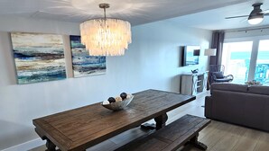 A dining area with a wooden table and bench, a chandelier, and artwork on the walls. - 7B - 2BR $700+ in freebies incl golf, On Beach (Miramar Beach)