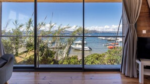 A room with large windows offering a view of a marina with boats and mountains.