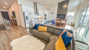 Ein modernes Wohnzimmer mit einer Eckcouch, einem weißen, flauschigen Teppich und einem Essbereich mit großem Fenster.