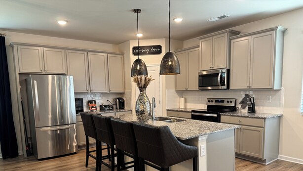 A modern kitchen with a central island, bar stools, stainless steel appliances, and pendant lighting. - Chic Family Home Near All ATL Hotspots (Atlanta)