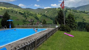 A swimming pool with a wooden fence, surrounded by a grassy area and a mountainous landscape in the background. - Engel Ingold Lodge-Romantic place in the middle of the Swiss Alps-Hotel Services (Habkern)