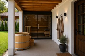 Un sauna en bois avec une porte en verre, une plante en pot et un porte-serviettes fixés au mur extérieur.