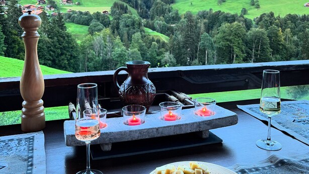 A table set with glasses, a candle, a pitcher, and a plate of food, overlooking a mountainous landscape. - Engel Ingold Lodge-Romantic place in the middle of the Swiss Alps-Hotel Services (Habkern)