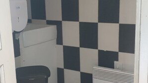 Une petite salle de bain avec des toilettes blanches, une poubelle noire, un radiateur blanc et un mur à carreaux noirs et blancs.