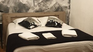 Un lit bien fait, avec une tête de lit en bois, un coussin aux motifs noir et blanc et une serviette blanche posée sur le lit.