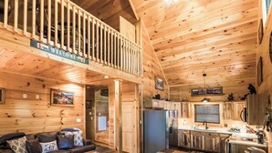 Ein Holzblockhaus-Interieur mit Balkon, einer Küchenzeile und einem Wohnzimmer mit einer Couch.