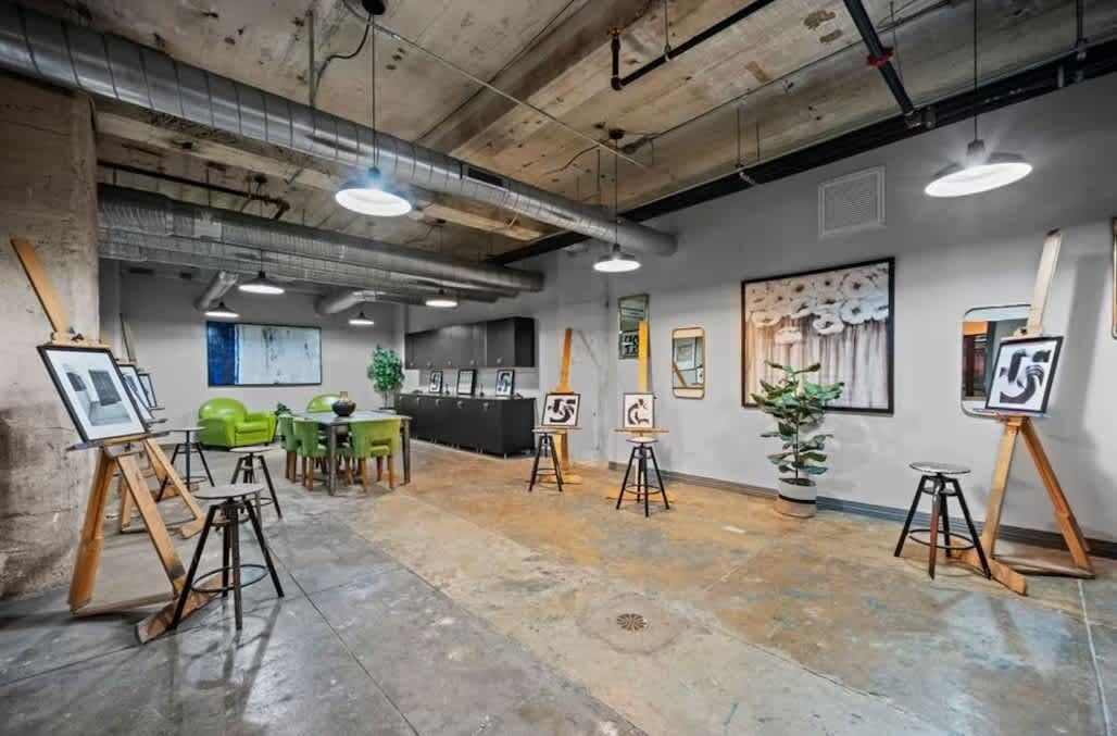 Une galerie d’art où des chevalets présentent des tableaux, un comptoir d’accueil et des chaises vertes.
