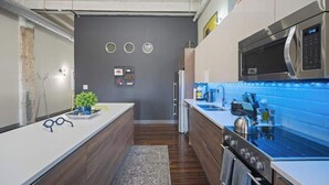 A modern kitchen with a central island, stainless steel appliances, and a blue backsplash. - The Bentley Collection - Downtown Penthouse Close to Convention Center (Dallas)