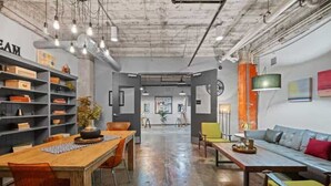 An open-plan office with a long wooden table, chairs, a sofa, and shelves with books and decorative items. - The Bentley Collection - Downtown Penthouse Close to Convention Center (Dallas)