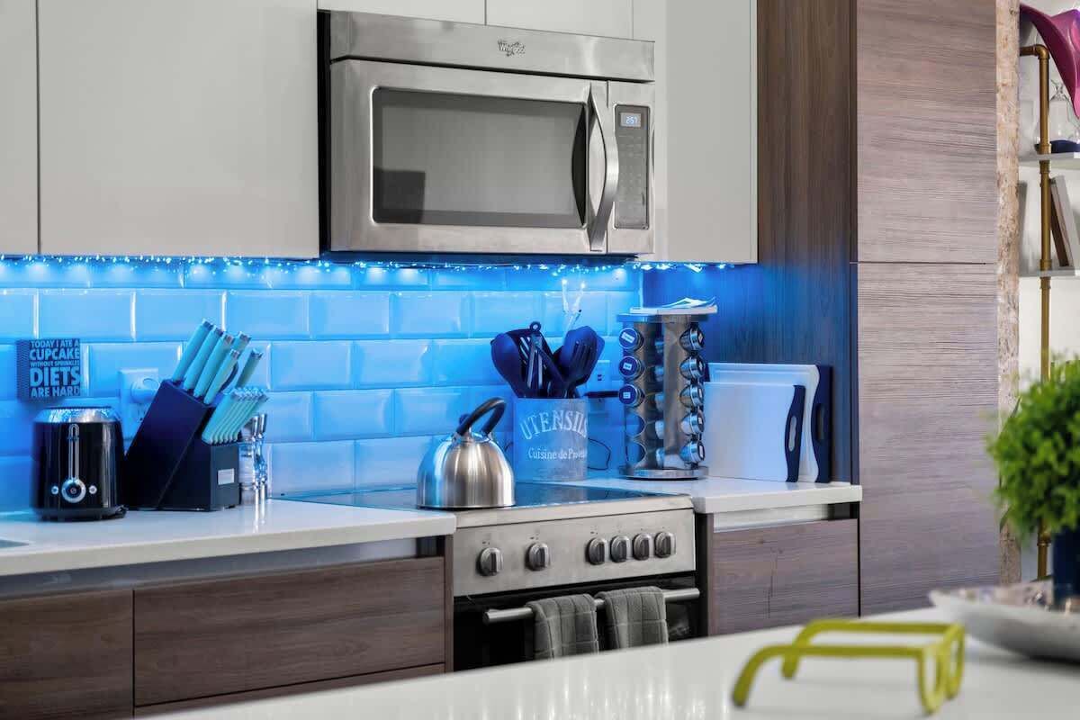 A modern kitchen with a stainless steel microwave, a kettle, and a set of knives on the counter.