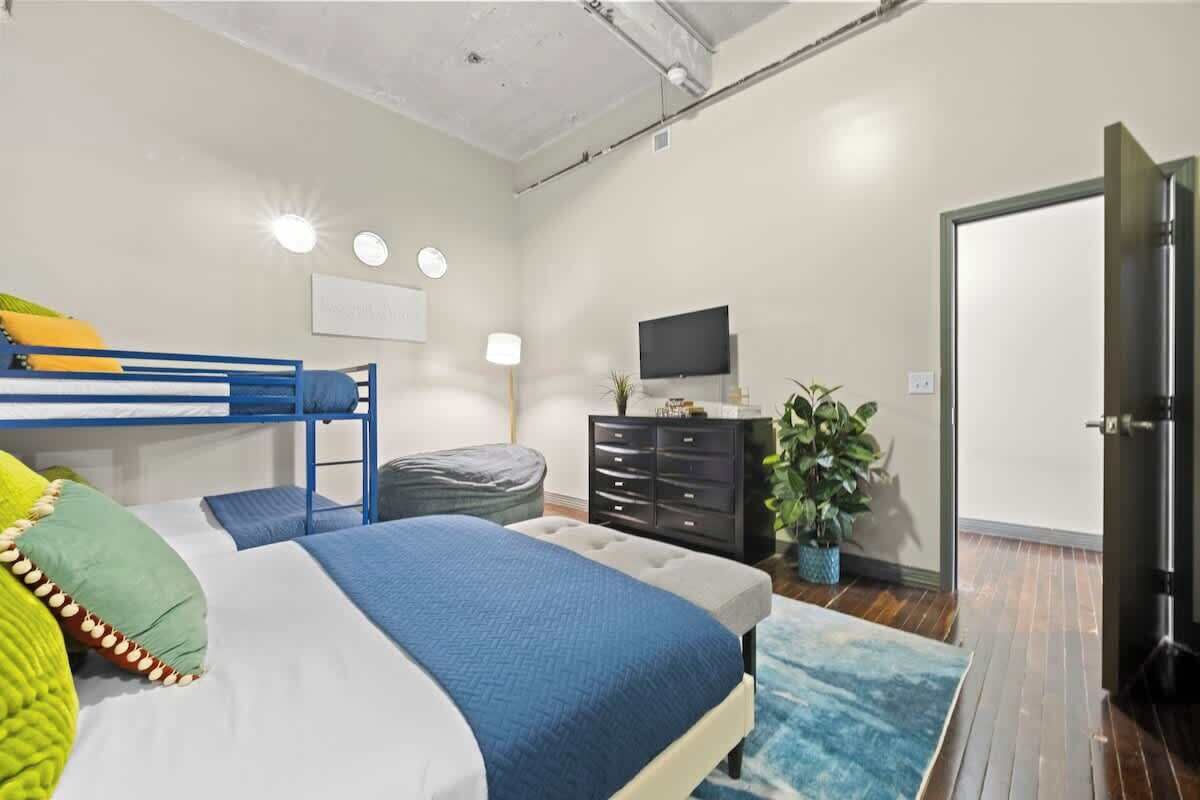 Une chambre avec un lit superposé, un téléviseur à écran plat, une commode et une plante en pot.