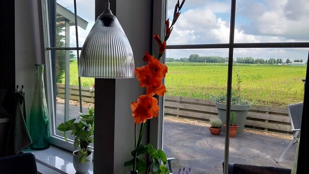 A dining area with a table, candles, and a view of a green field through large windows. - Cozy and fully furnished apartment centrally located between Enkhuizen and Hoorn (Hem)