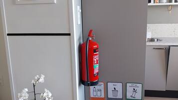 Een kamer met een deur, een aan de muur bevestigde brandblusser, een prullenbak en recyclingbakken.