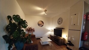 A living room with a sofa, coffee table, TV, and a large plant. - Cozy and fully furnished apartment centrally located between Enkhuizen and Hoorn (Hem)
