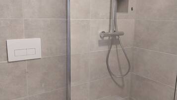 A modern bathroom with a glass-enclosed shower, a toilet, and a wall-mounted flush handle.