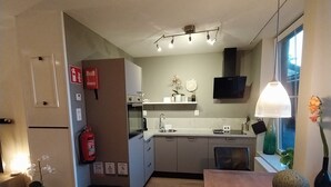 A modern kitchen with a built-in oven, a sink, and a microwave. There is a dining table with a vase and a lamp. The room has a wooden floor and a window with a view. - Cozy and fully furnished apartment centrally located between Enkhuizen and Hoorn (Hem)