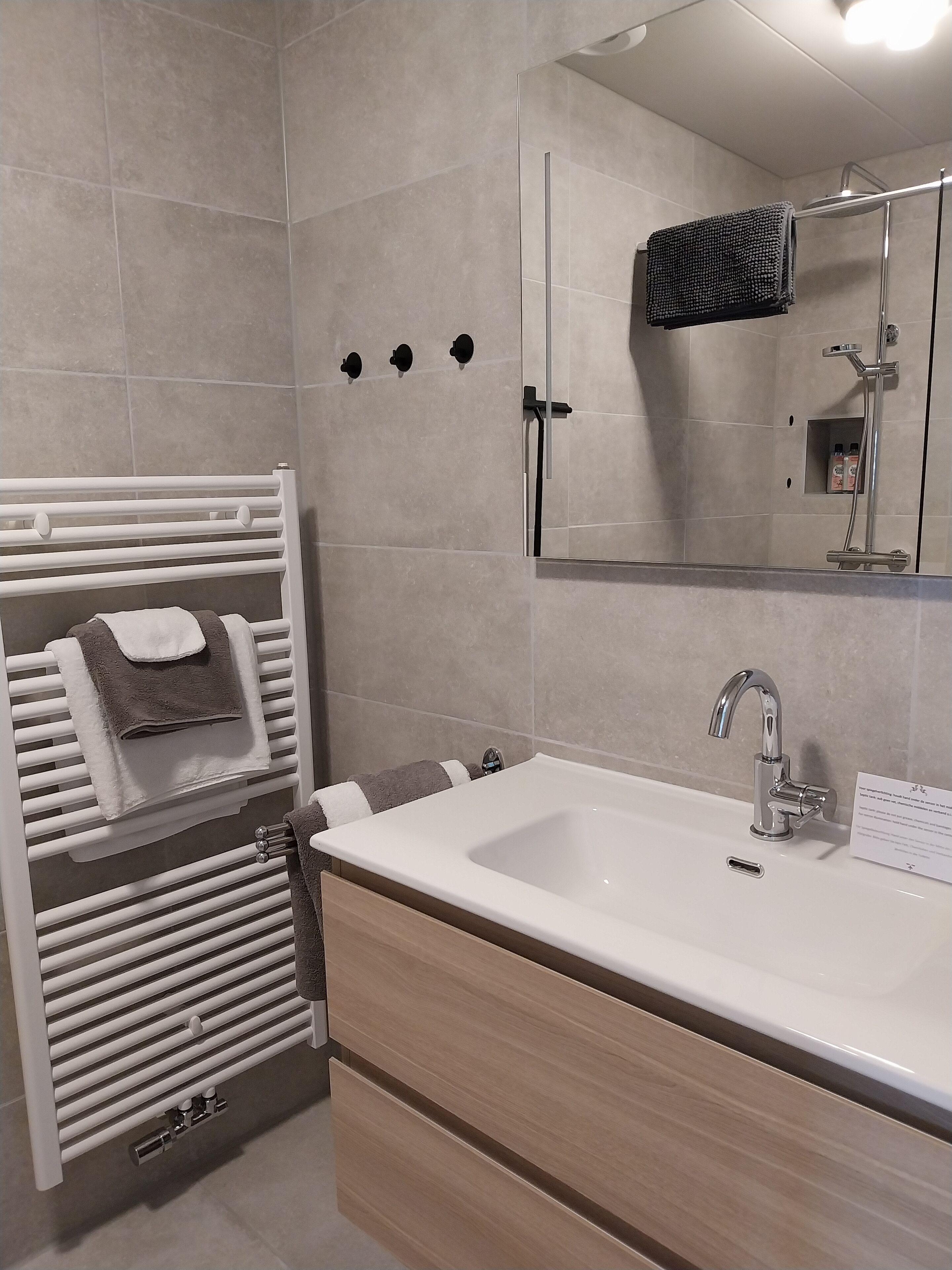 Ein modernes Badezimmer mit einem weißen Waschbecken, einem Spiegel und einem Handtuchhalter mit Handtüchern.