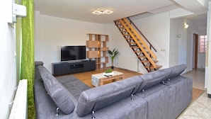 A modern living room with a grey sofa, a TV, wooden shelves, and a staircase. - Idyllic Escape in Fasana, Relax and Unwind (Fazana)
