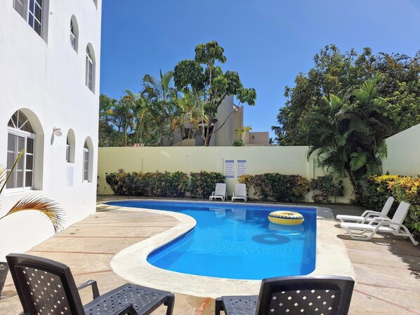 Relax by the serene pool surrounded by lush greenery and a beautiful building with arched windows.