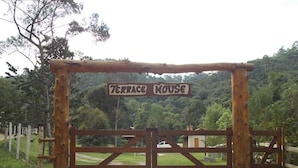 Una puerta de madera con un letrero que dice 'Terrace House' frente a un exuberante paisaje verde.