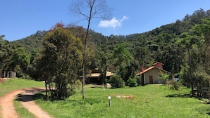Paisaje rural con un sendero de tierra que lleva a una casa rodeada de árboles y colinas.
