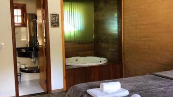 Quarto de hotel com cama, banheiro com banheira e uma pequena cozinha.