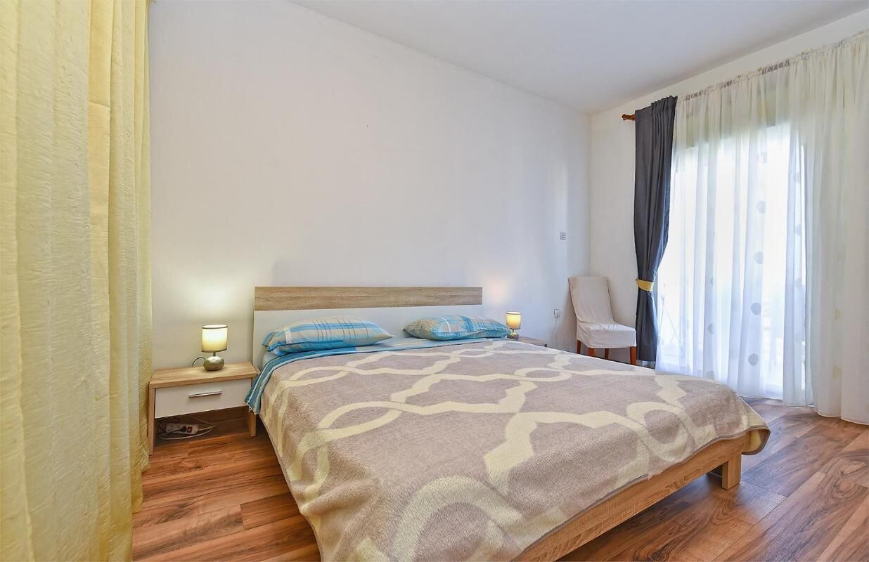 A bedroom with a wooden bed, bedside lamps, a chair, and a window with curtains.