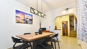 A dining area with a wooden table and black chairs, a vase with dried plants, and a painting of a sunset. - Stylish Family Retreat With Shared Pool (Fazana)