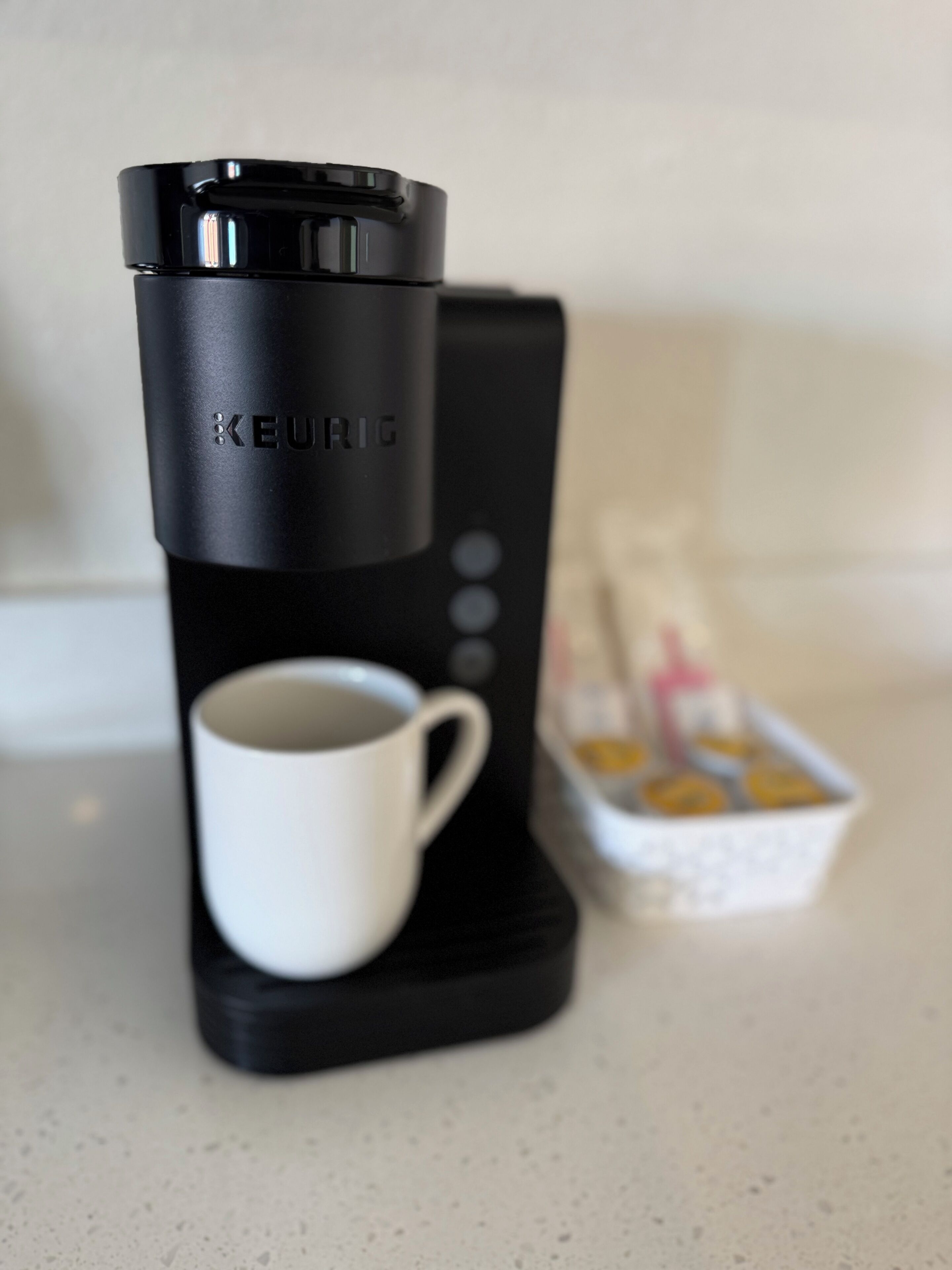 A Keurig coffee maker with a white mug and a box of coffee pods on a countertop.
