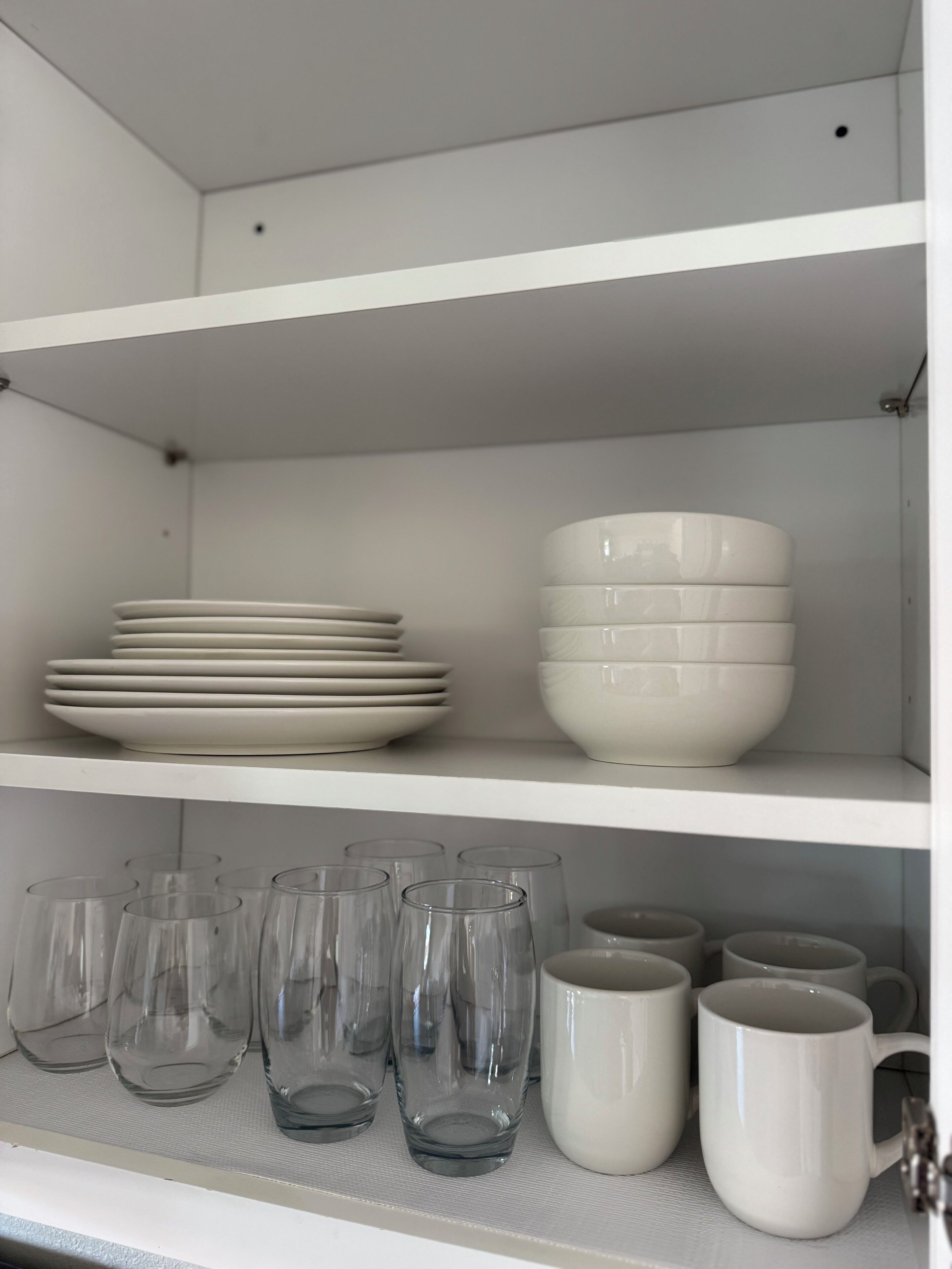 A white shelving unit with stacked plates, bowls, and clear glassware.