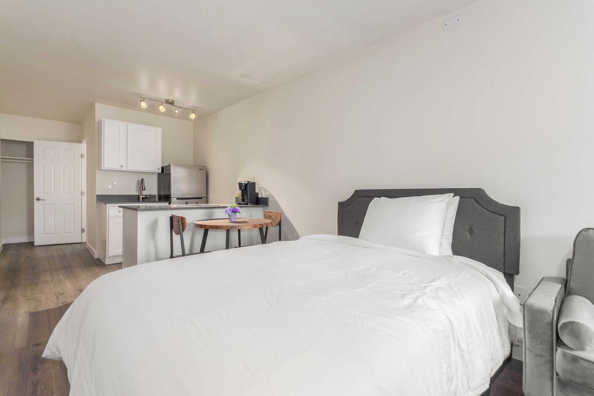 Habitación de hotel con cama, una pequeña mesa de trabajo con silla, kitchenette y una puerta blanca.