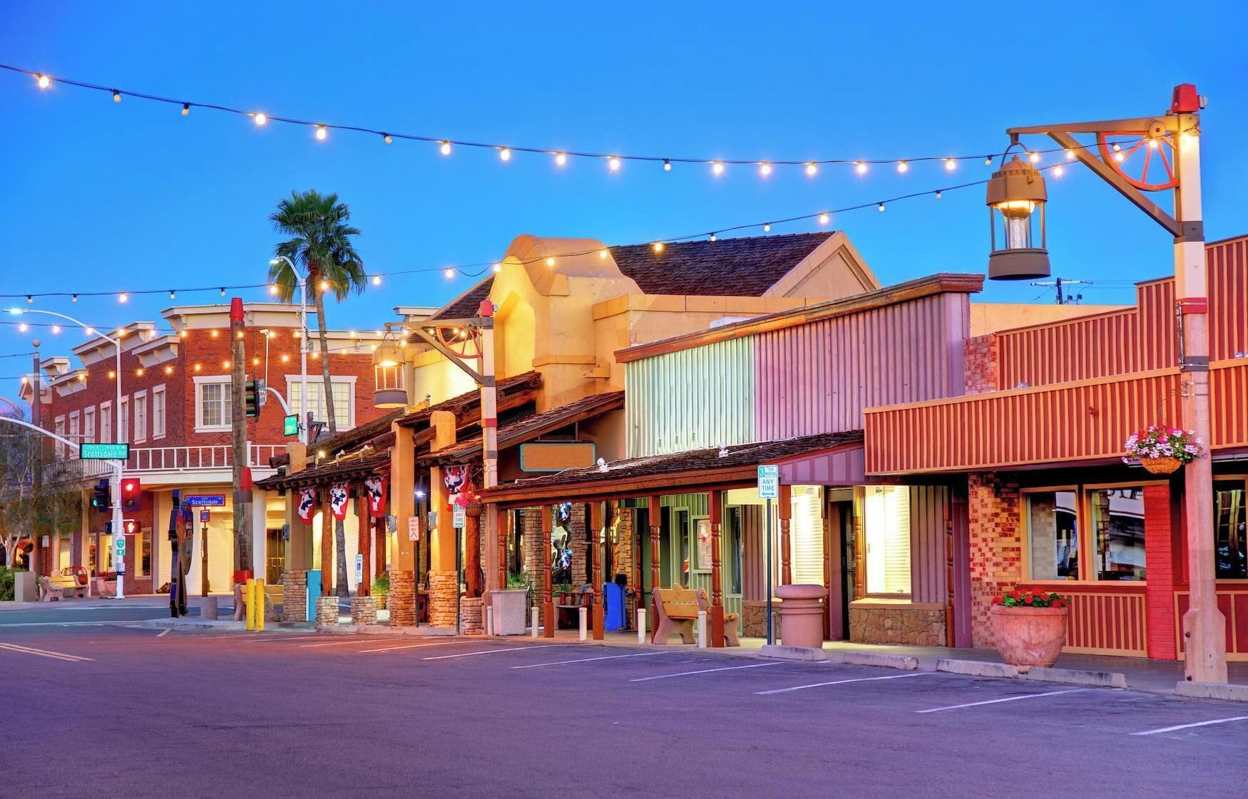 A street lined with colorful buildings, some with outdoor seating and string lights.