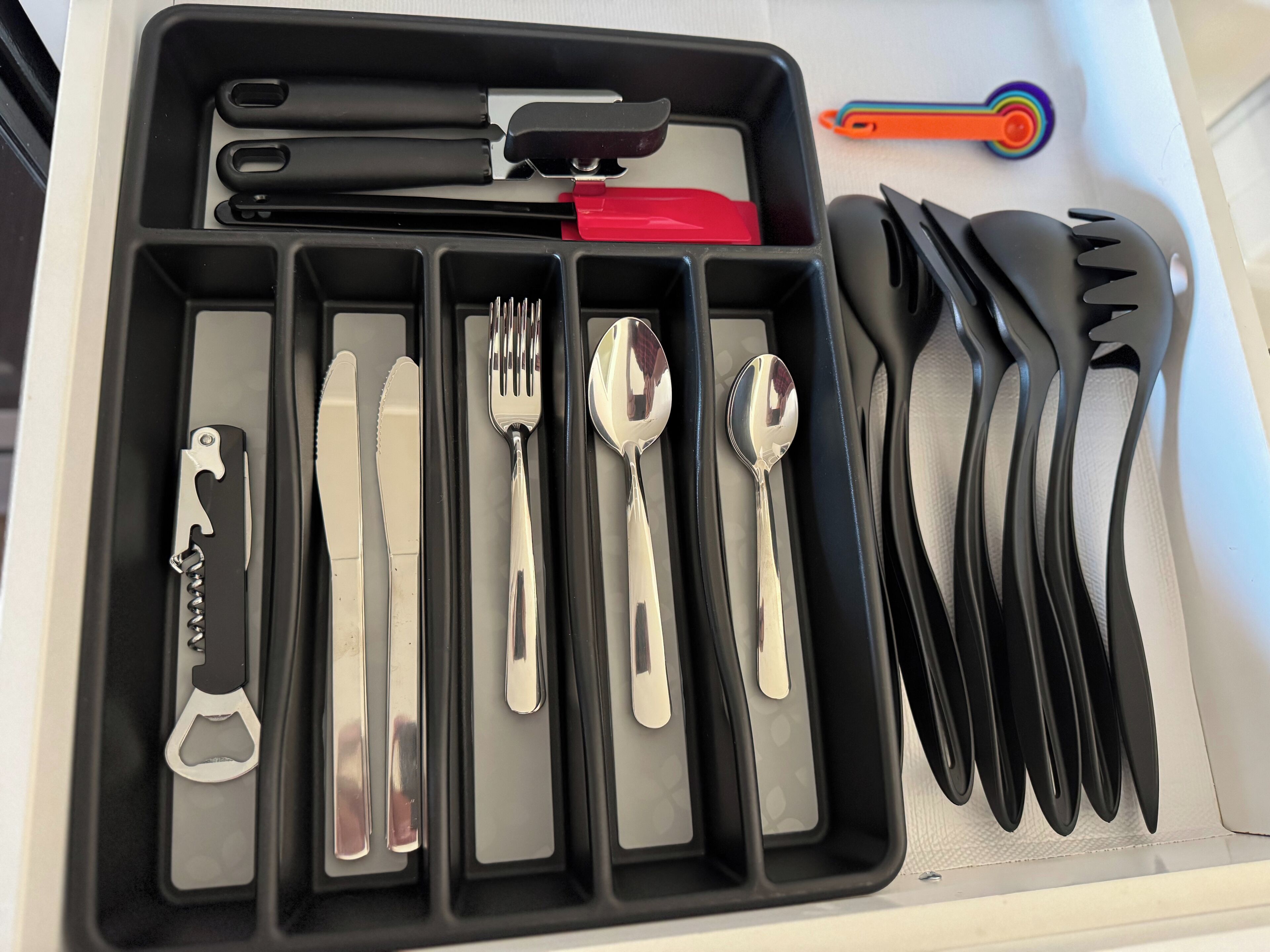 Een zwarte organizer met vakken, gevuld met verschillende keukengerei zoals een mes, vork, lepel en een flesopener.