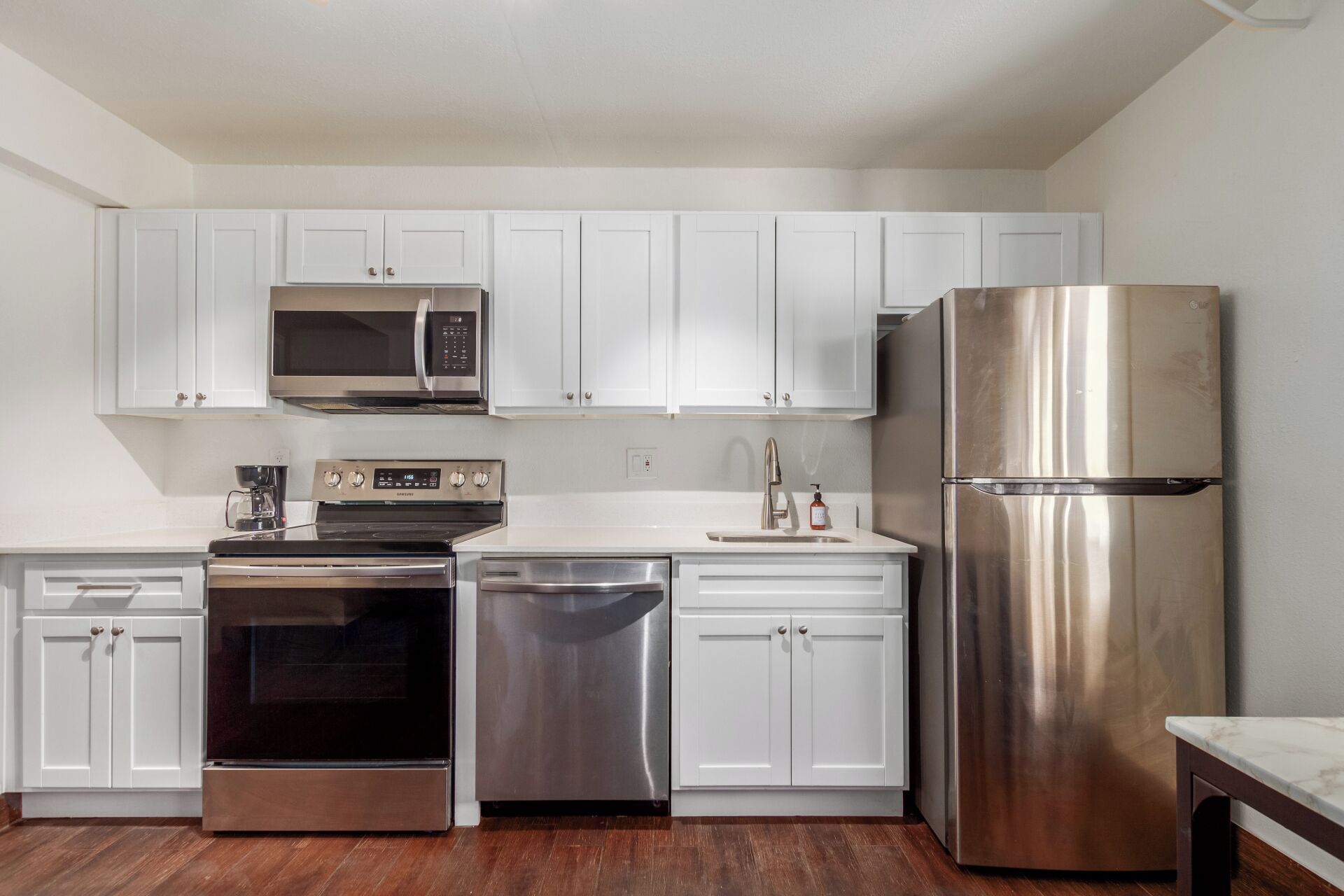 A modern kitchen with white cabinets, stainless steel appliances, and a wooden floor.